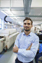 Young businessman standing with arms crossed at illuminated factory - MOEF03417