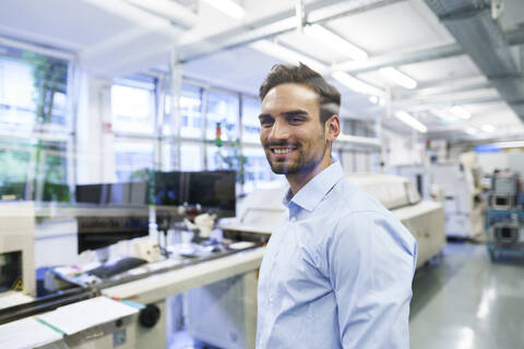 Smiling young male technician standing at illuminated factory stock photo