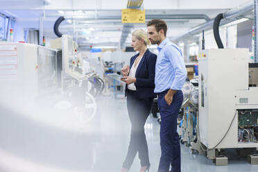 Mature businesswoman holding digital tablet while standing with young colleague at illuminated factory - MOEF03422