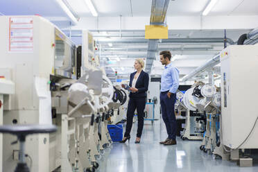 Männlicher Techniker steht neben einer Geschäftsfrau, die in einer Fabrik Maschinen analysiert - MOEF03428