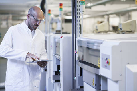 Mature male technician using digital tablet while examining machinery at laboratory stock photo