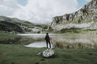 Woman with hands in pockets standing against lake - GMLF00646