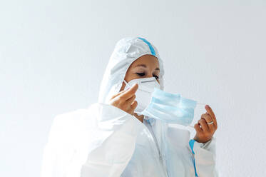 Nurse in protective workwear wearing face mask while standing against white wall - PGF00092