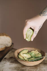 Frau drückt mit der Hand eine Limette in einen Avocadosalat, der auf einem Schneidebrett in der Küche aufbewahrt wird - ALBF01549