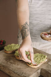 Junge Frau garniert Guacamole auf gebackenem Brot, während sie in der Küche zu Hause steht - ALBF01552