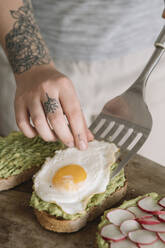 Woman garnishing omelet on guacamole spread bread while standing at kitchen - ALBF01553