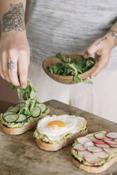 Junge Frau garniert Guacamole-Brot mit Gurke und Blatt in der Küche - ALBF01554