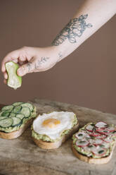 Frau drückt Limette auf Brot, das mit Gemüse und Guacamole auf einer Servierplatte in der Küche garniert ist - ALBF01557