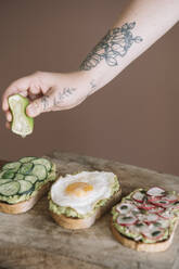 Woman squeezing lime on bread garnished with vegetable and guacamole on serving dish at kitchen - ALBF01557