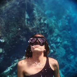 Young female diver in swimsuit and snorkeling mask floating in clean transparent sea water - ADSF15686