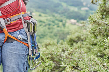 Unbekannter männlicher Kletterer mit Sicherheitsausrüstung und Karabinern klettert vor dem Hintergrund eines grünen Waldes - ADSF15690