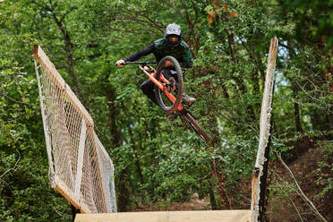 Low angle of brave male in helmet performing extreme trick on bicycle for downhill in woods - ADSF15691