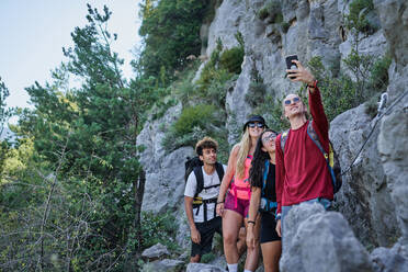 Gruppe freundlicher Touristen mit Rucksäcken, die im Hochland stehen und ein Foto mit der Selfie-Kamera während des Urlaubs machen - ADSF15698