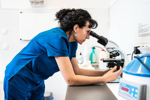 Eine Ärztin schaut durch ein modernes Mikroskop, das auf einem Tisch im Labor einer modernen Klinik steht - ADSF15768