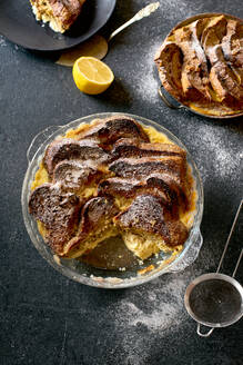 Draufsicht auf traditionellen Brotpudding mit Pudding, serviert mit aromatischer Orangenzestenbutter und Puderzucker auf dunklem Hintergrund - ADSF15774
