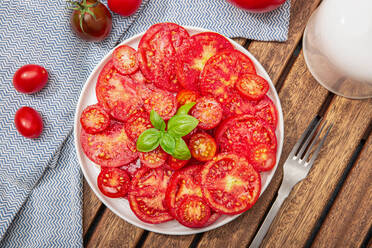 Draufsicht auf Tomatensalat und Basilikumblätter auf einem Teller. Mediterranes Essen - ADSF15799