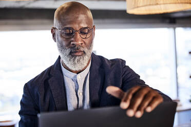 Serious mature man working on laptop sitting at home - FMKF06332