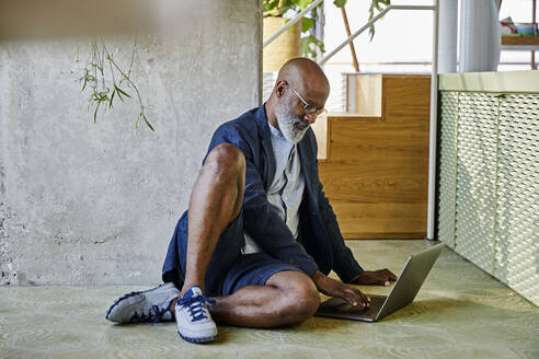 Reifer Mann arbeitet am Laptop, während er zu Hause sitzt - FMKF06340
