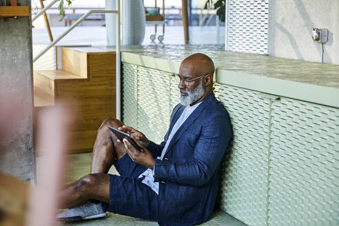 Reifer Mann, der ein digitales Tablet benutzt, während er zu Hause sitzt - FMKF06341