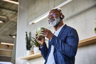 Man listening to music while drinking coffee looking away at home - FMKF06354