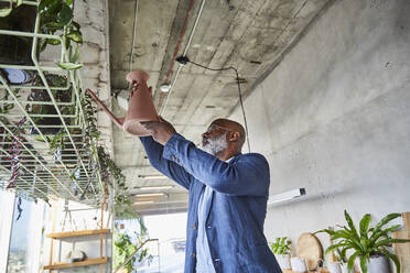 Mature man watering houseplant while standing at home - FMKF06356