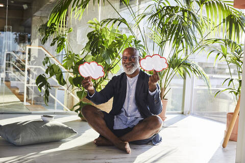 Smiling man holding thought bubble with cross leg sitting at home stock photo