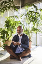 Mature man holding bowl while sitting at home - FMKF06365