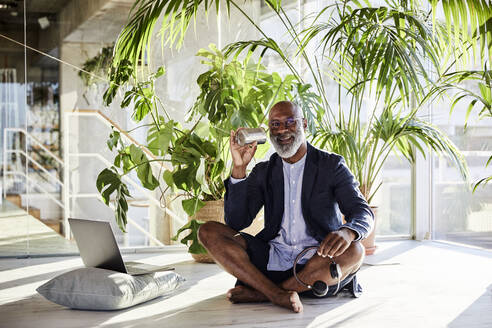 Mature man using tin can phone while holding headphone sitting at home - FMKF06369