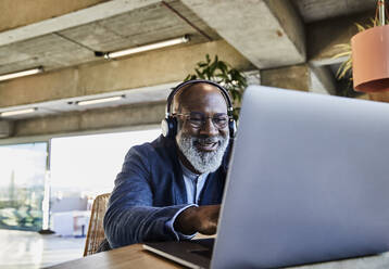 Geschäftsmann lächelnd bei der Arbeit am Laptop zu Hause - FMKF06382