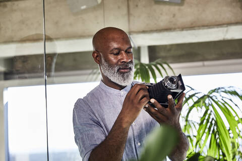 Mature man using digital camera while standing at home stock photo