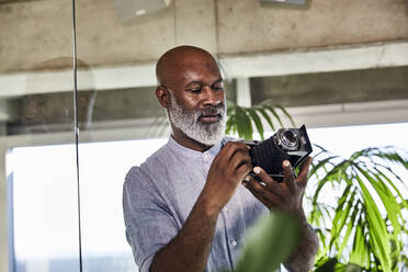 Älterer Mann, der eine Digitalkamera benutzt, während er zu Hause steht - FMKF06383
