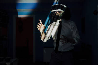 Man using virtual reality glasses while standing at home during pandemic - MRRF00487