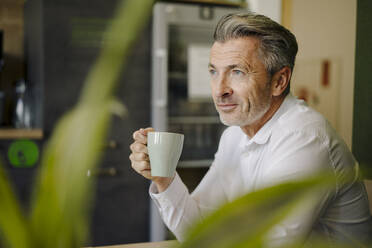 Mann trinkt Kaffee und sitzt am Tisch im Büro - JOSEF01969