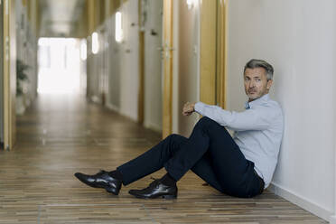 Man sitting on floor at corridor in office - JOSEF01971