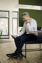 Mann, der ein digitales Tablet benutzt, während er am Tisch im Büro sitzt - JOSEF01978
