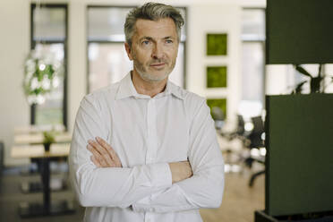 Confident businessman standing with arms crossed at office - JOSEF01981