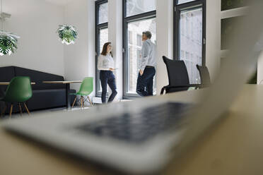 Geschäftsleute im Gespräch, während sie sich im Büro an die Wand lehnen - JOSEF01992