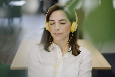 Woman relaxing while listening music at office - JOSEF01994