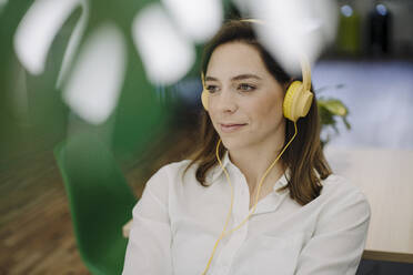 Smiling woman listening music while sitting in office - JOSEF01996