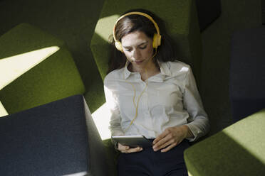 Woman with headphones using digital tablet while relaxing on floor in office - JOSEF01999