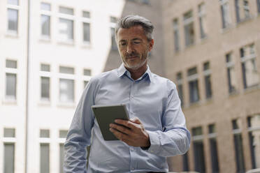 Geschäftsmann, der ein digitales Tablet benutzt, während er an einem Gebäude steht - JOSEF02009