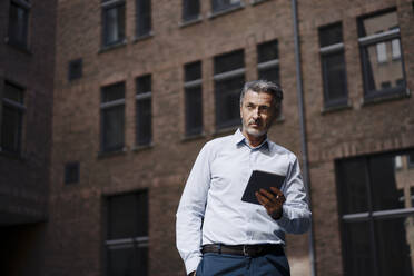 Geschäftsmann schaut weg, während er ein digitales Tablet gegen ein Gebäude benutzt - JOSEF02017
