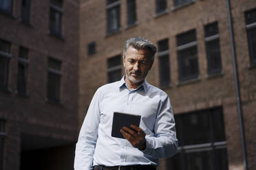 Geschäftsmann hält digitales Tablet, während er an einem Gebäude steht - JOSEF02018