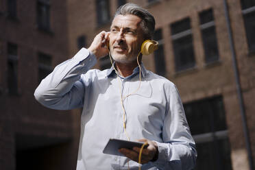 Businessman with headphones using phone while standing against building - JOSEF02020