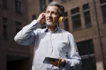 Geschäftsmann mit Kopfhörern telefoniert im Stehen an einem Gebäude - JOSEF02020