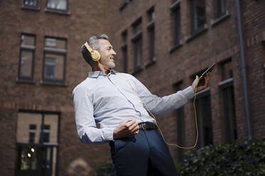 Carefree businessman dancing while listening music against building - JOSEF02024