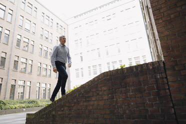 Businessman walking on staircase against building - JOSEF02030