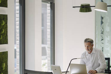 Man working on laptop while sitting by desk at office - JOSEF02047