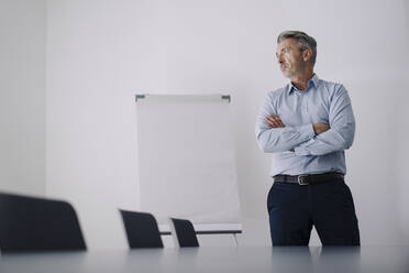 Businessman with arms crossed standing in board room at office - JOSEF02064