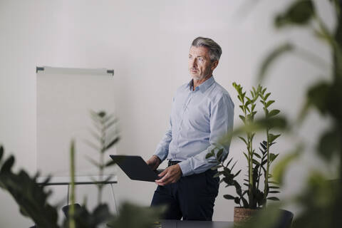 Businessman holding laptop while standing at office stock photo